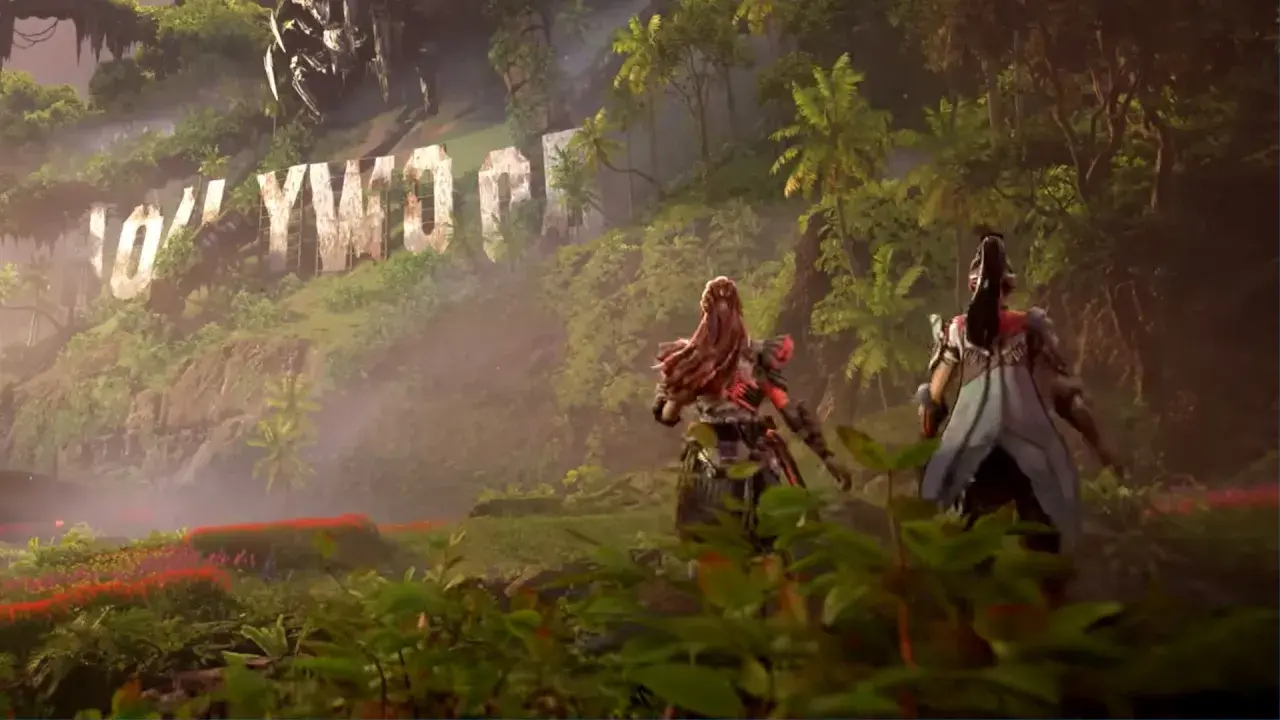 Aloy i jej towarzyszka przemierzają bujną dżunglę w Horizon Forbidden West: Burning Shores, mijając zniszczony napis Hollywood.