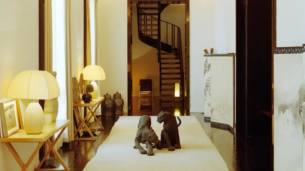 Due sculture di pantere su un tappeto chiaro, in un corridoio elegante che ricorda la casa Giorgio Armani, con una scala a chiocciola sullo sfondo.