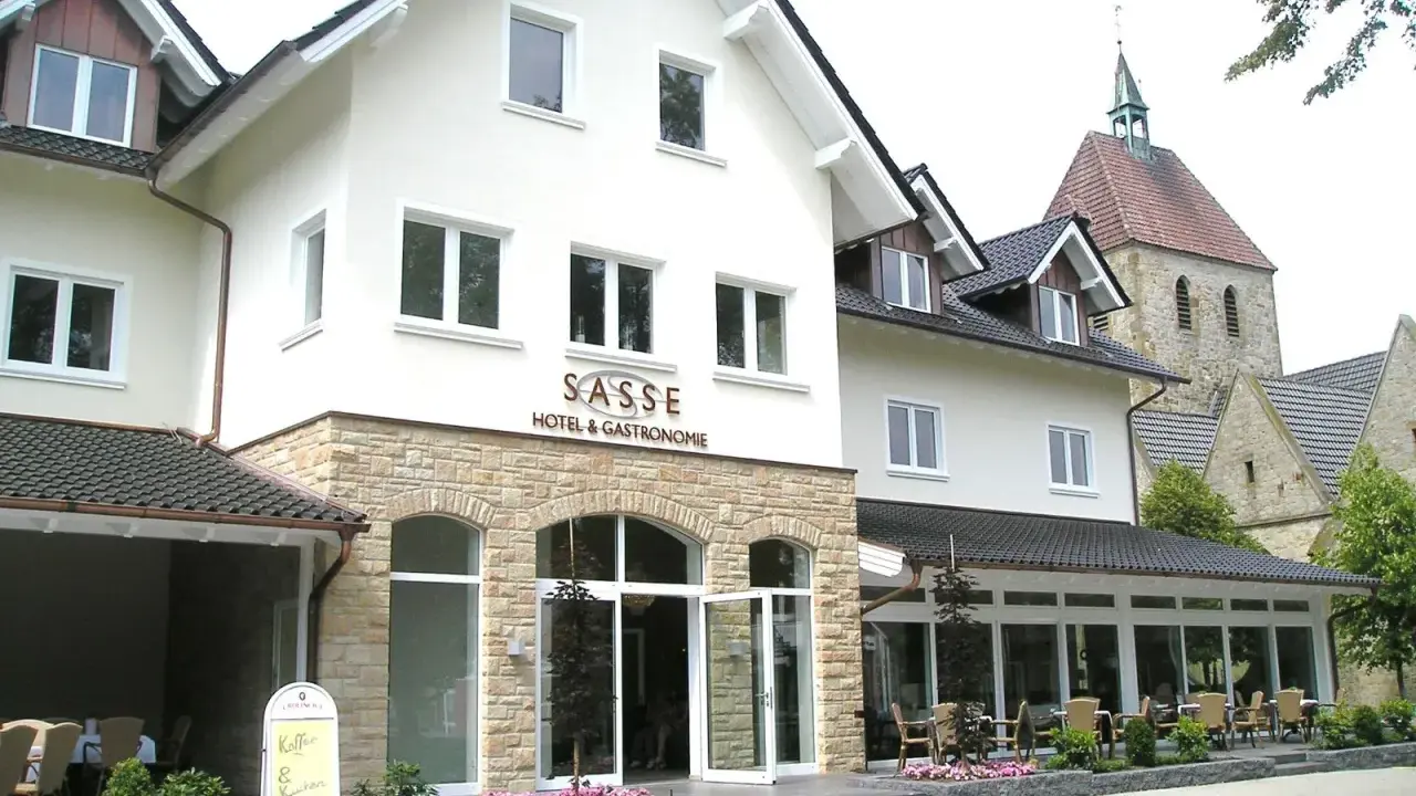 Gasthof Sasse in Soest mit Hotel & Gastronomie-Schild, Steinfassade und Kirche im Hintergrund.