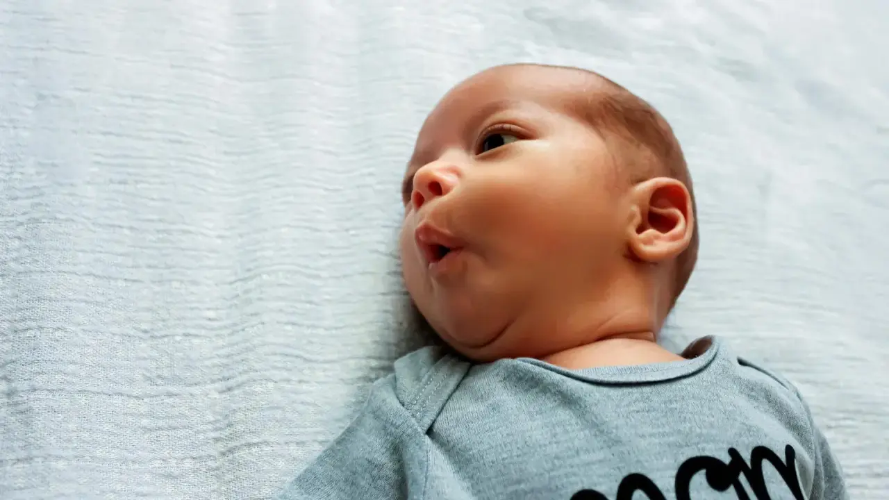 Noworodek z lekkim kręczem szyi i asymetrią twarzy, w szarym body z napisem "mom".