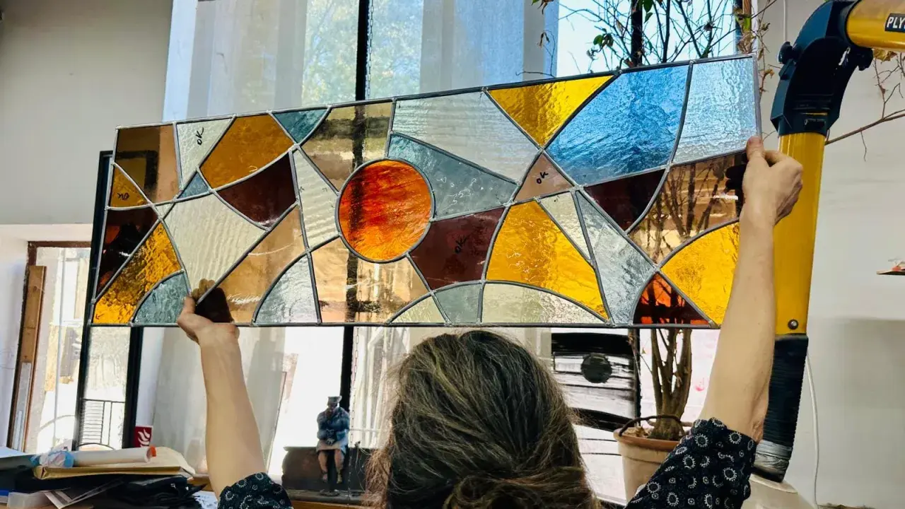Un artiste admire son œuvre, un vitrail aux couleurs chaudes et géométriques, fruit d'un cours de vitrail.