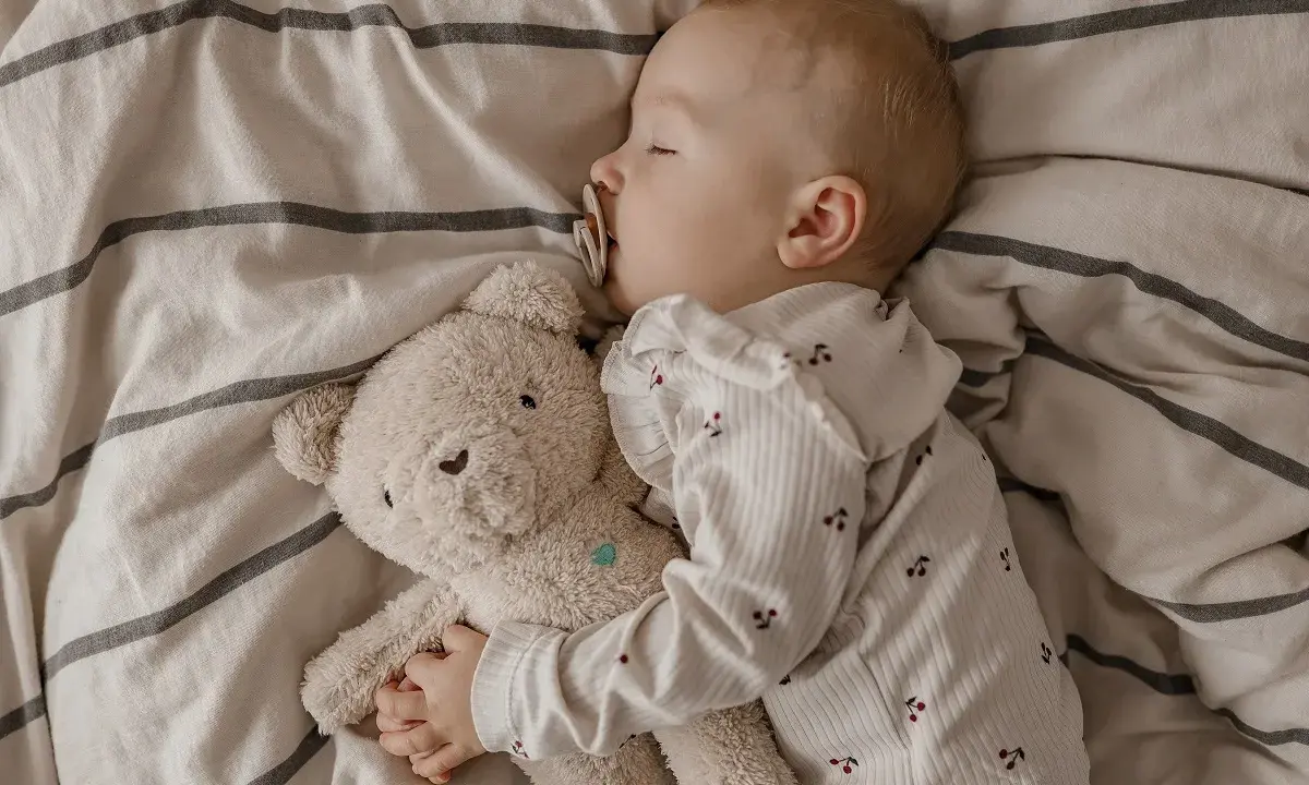Kleines Kind schläft friedlich mit Teddybär. Die **Schlafregression 1 Jahr** ist eine Herausforderung, aber dieser süße Anblick tröstet.