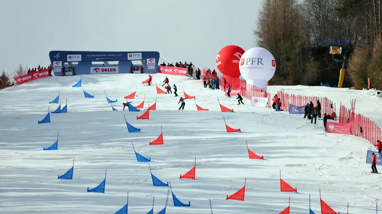 Zawodnicy snowboardu pokonują trasę z czerwonymi i niebieskimi tyczkami na stoku Jaworzyny Krynickiej.