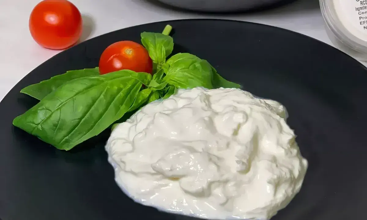 En krämig hög av stracciatella ost med färska basilikablad och körsbärstomater på en svart tallrik.