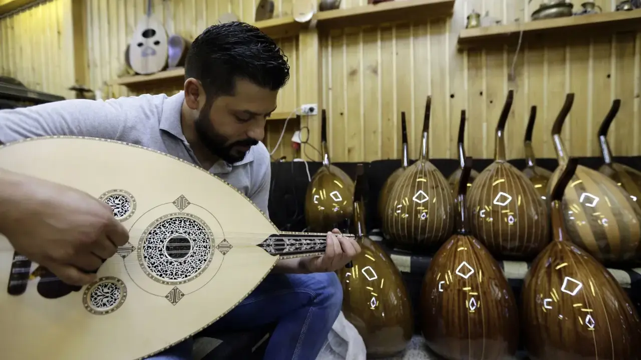 Un joueur de oud expérimenté accorde son instrument, entouré d'autres ouds prêts à être joués.