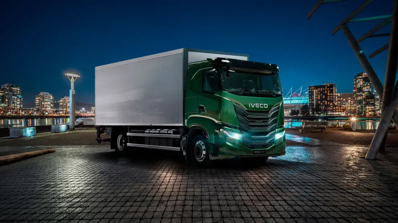 Camión Iveco S-Way V8 780 verde brillante aparcado en un muelle urbano de noche, con luces de ciudad al fondo.