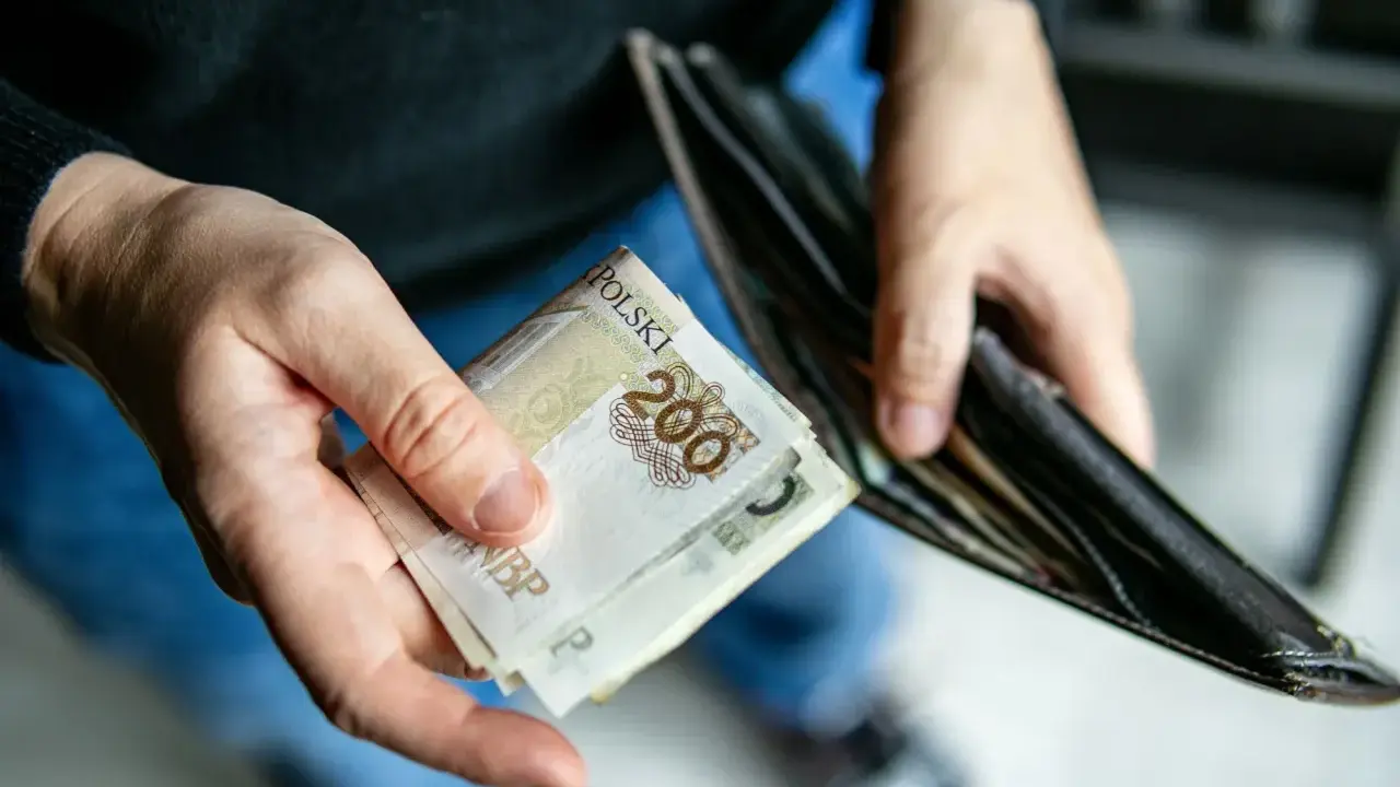 Dłonie trzymają banknoty 200 zł i pusty portfel. Może to symbolizować trudności finansowe i potrzebę wsparcia z opieki społecznej.