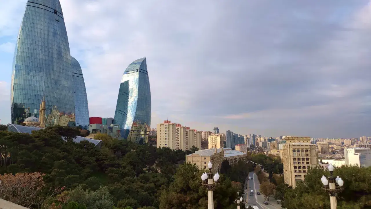 Płomienne wieże Flame Towers w Baku, które warto zobaczyć, górują nad miastem. W tle widać panoramę miasta i zielone drzewa.