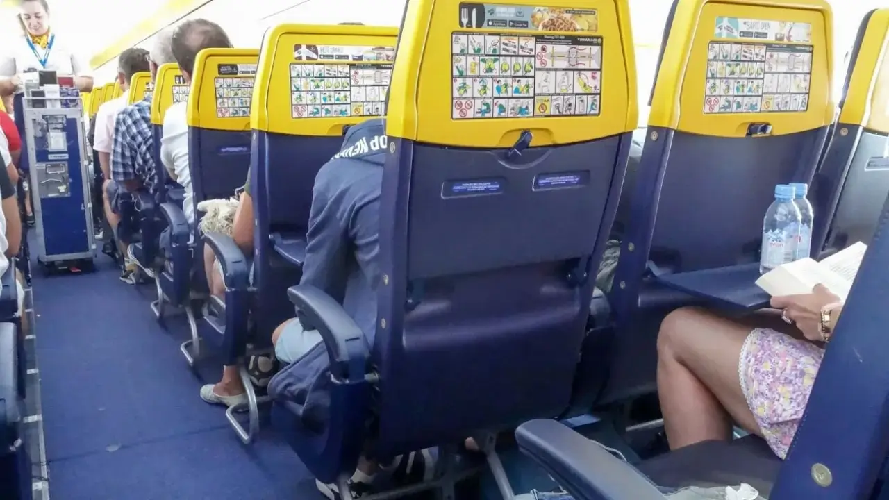 Wnętrze samolotu Boeing 737, rzędy miejsc dla pasażerów. Widok na siedzenia z żółtymi oparciami i instrukcjami bezpieczeństwa.