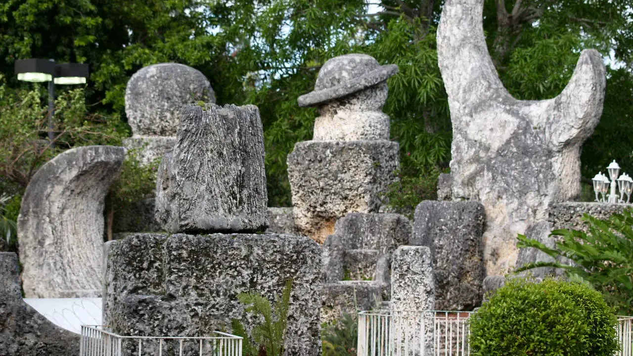 Sculture in pietra calcarea e corallo, tra cui un cappello e una forma a mezzaluna, creano un magico coral castle immerso nel verde.