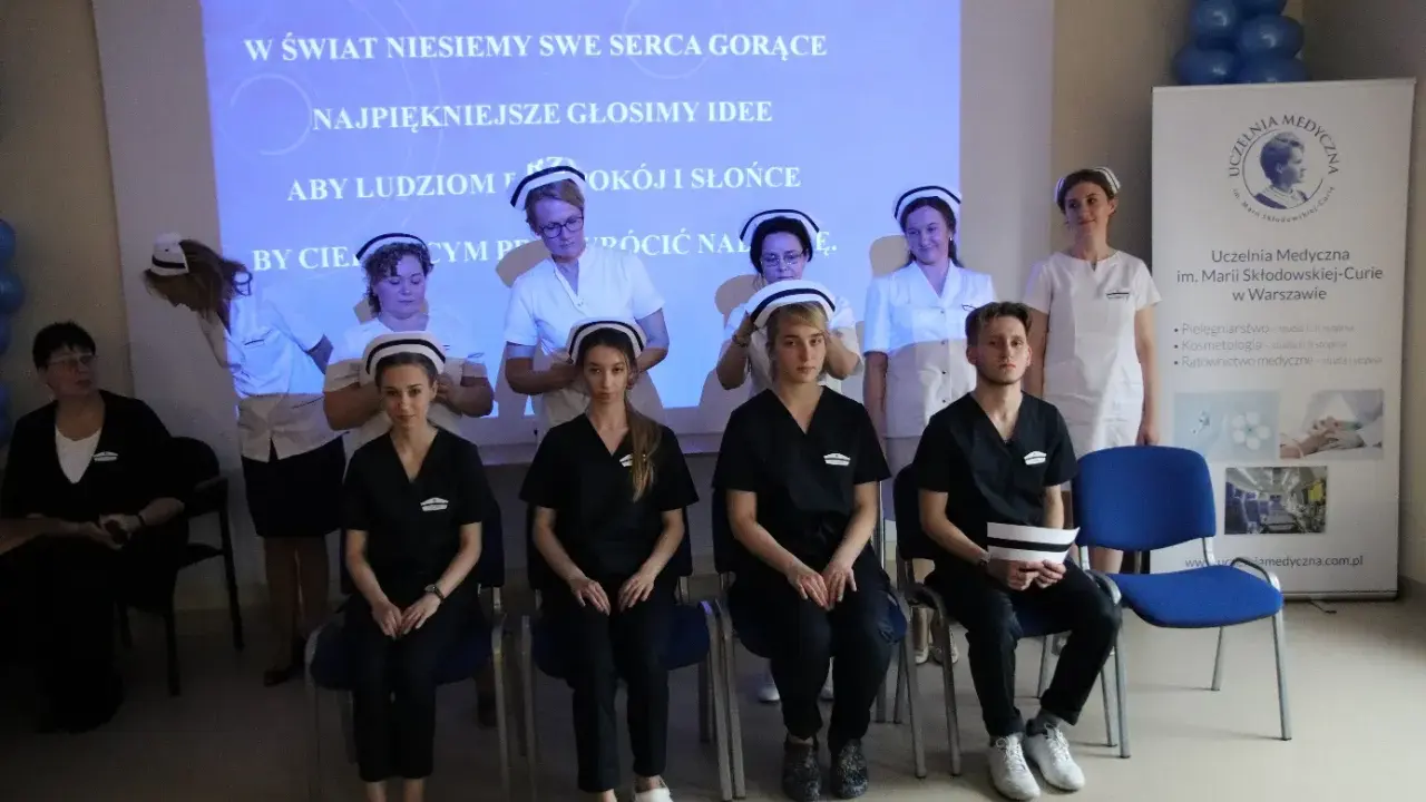 Uczelnia Medyczna im. Marii Skłodowskiej-Curie w Warszawie: studenci w strojach medycznych, z hasłem na ekranie.