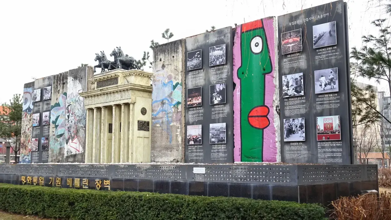 Fragment muru berlińskiego z graffiti i zdjęciami, obok replika Bramy Brandenburskiej.