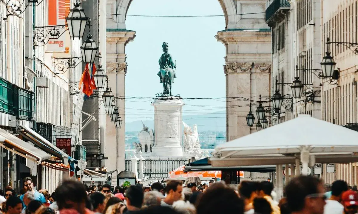 Menschenmenge auf der Rua Augusta in Lissabon mit Reiterstatue und Triumphbogen im Hintergrund.