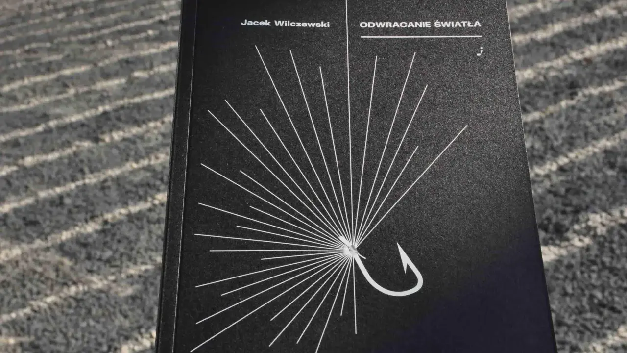 Okładka książki "Odwracanie światła" Jacka Wilczewskiego. Biały wzór przypominający promień słońca, z haczykiem wędkarskim w centrum. Nie ma przypadków, są tylko znaki.