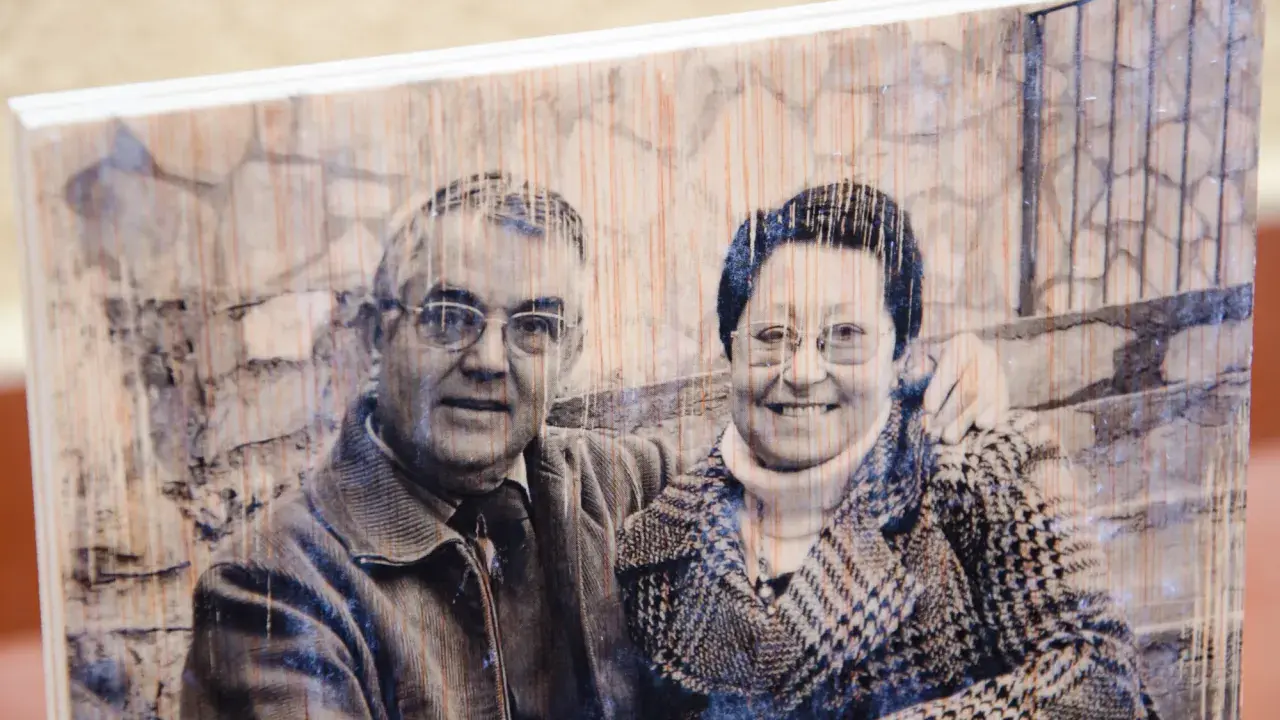Pareja sonriente en un retrato transferir foto a madera, con un fondo de ladrillos y textura de madera visible.