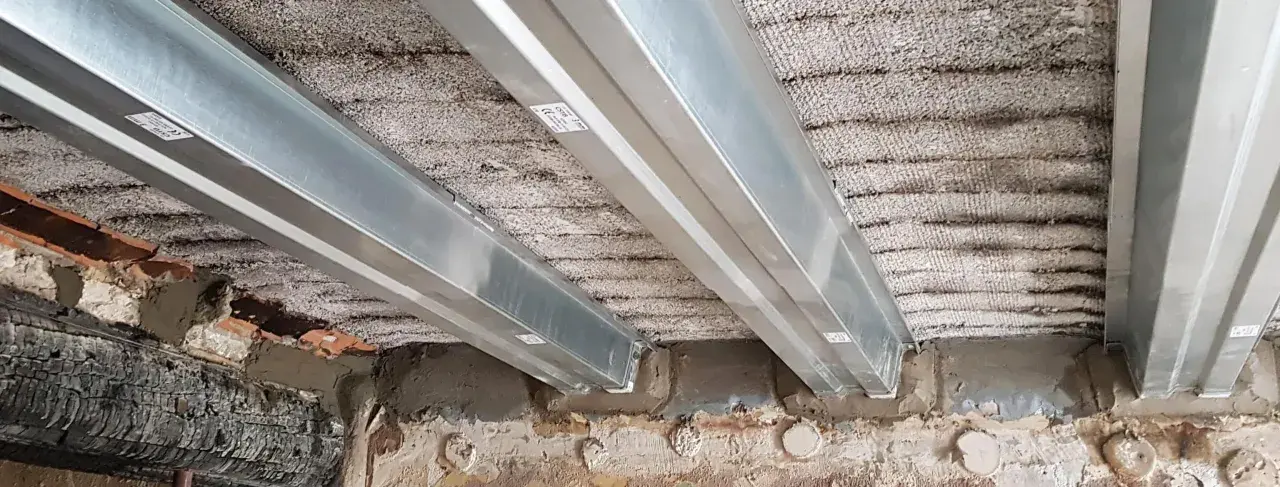 Vigas metálicas instaladas para como reforzar una viga de madera dañada por el fuego. Se observa el soporte de las nuevas vigas sobre la estructura existente.