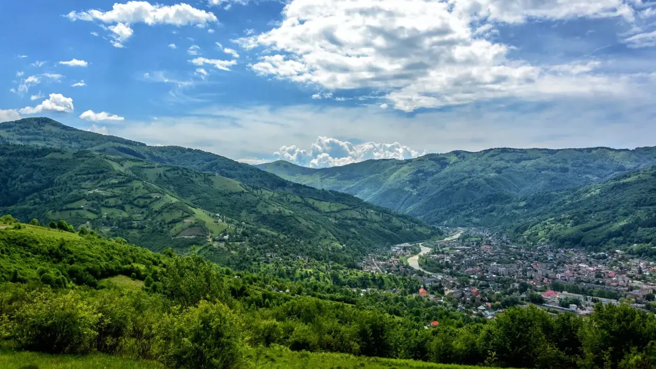 Zielone wzgórza Karpat na Ukrainie, z miasteczkiem w dolinie i rzeką.