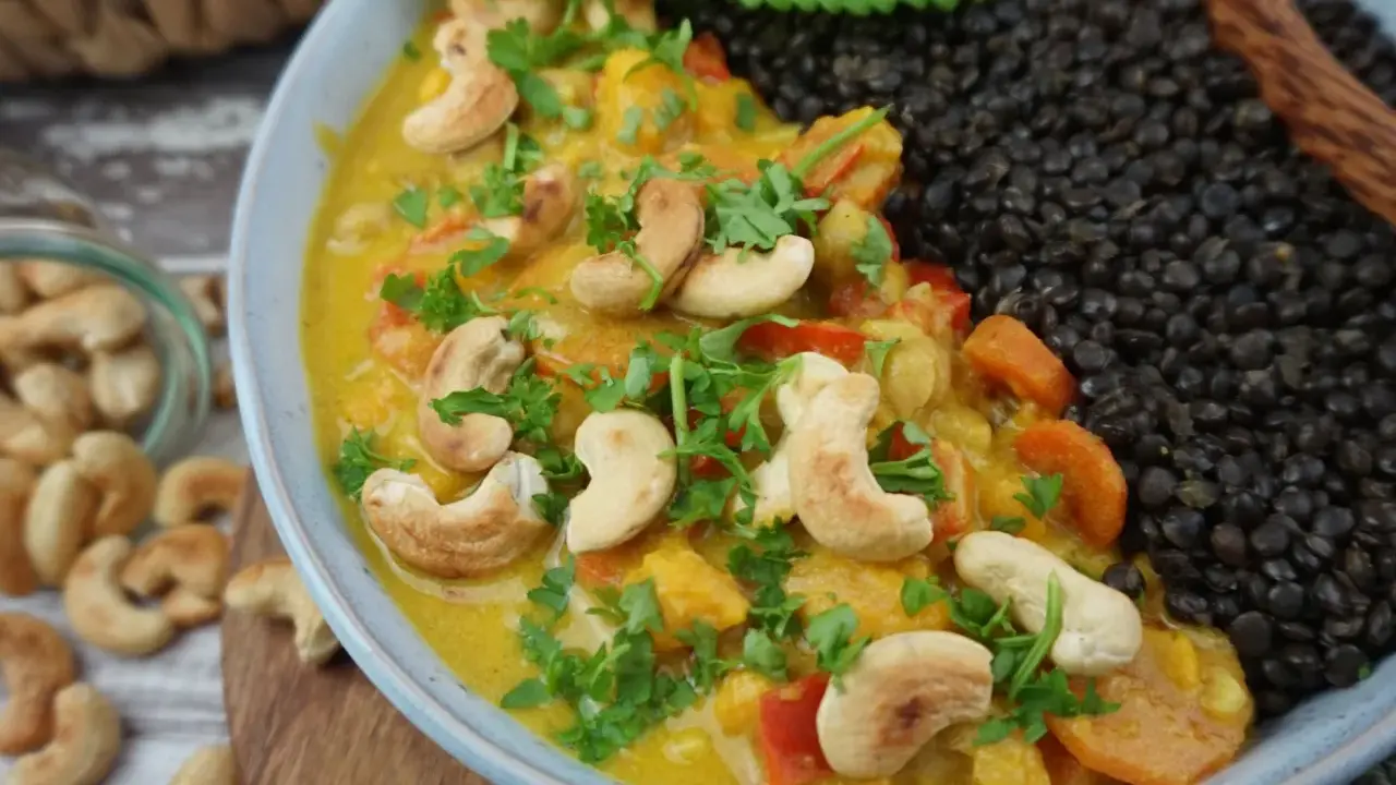 Ein cremiges Beluga Linsen Curry mit Cashewkernen und frischer Petersilie, daneben eine Portion schwarzer Beluga Linsen.