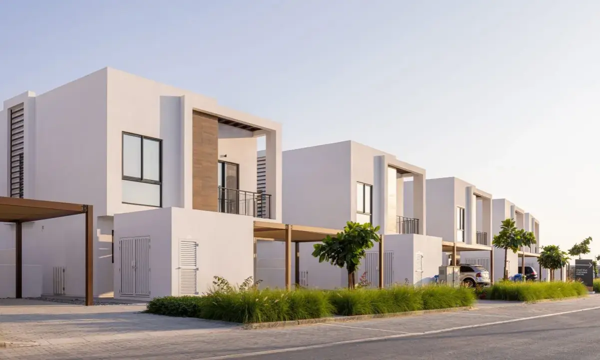 Frente fachadas de casas modernas con líneas limpias y detalles en madera. Un camino de adoquines y césped verde adornan el exterior.
