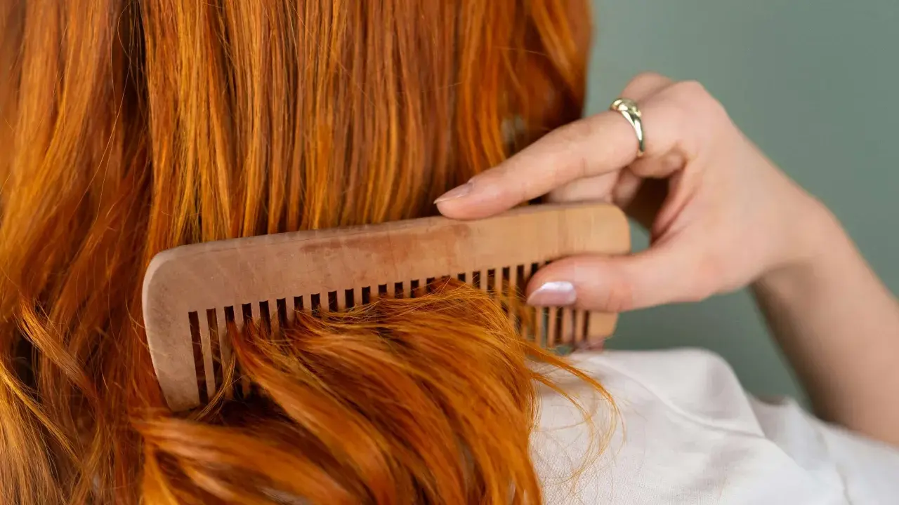 Mujer peina su cabello pelirrojo con un peine de madera. ¿En qué época del año se cae más el pelo? El otoño es conocido por ser el momento en que el cabello se cae más.