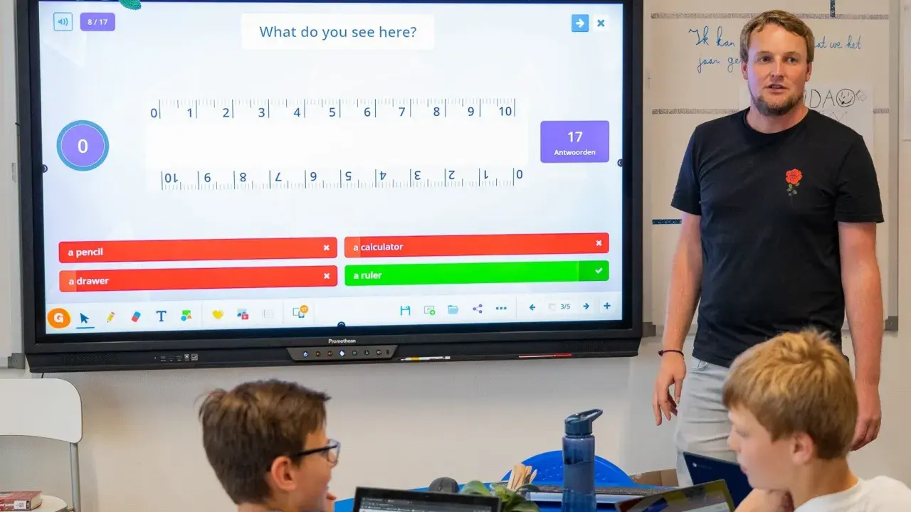 Un insegnante guida una lezione interattiva, simile a Kahoot, con domande su uno schermo touch. I bambini partecipano con entusiasmo.