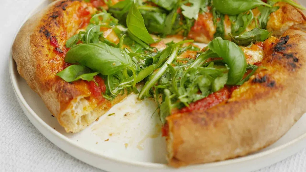 En närbild av en pizza med ruccola och basilika. Perfekt för ett enkelt pizzasås recept.