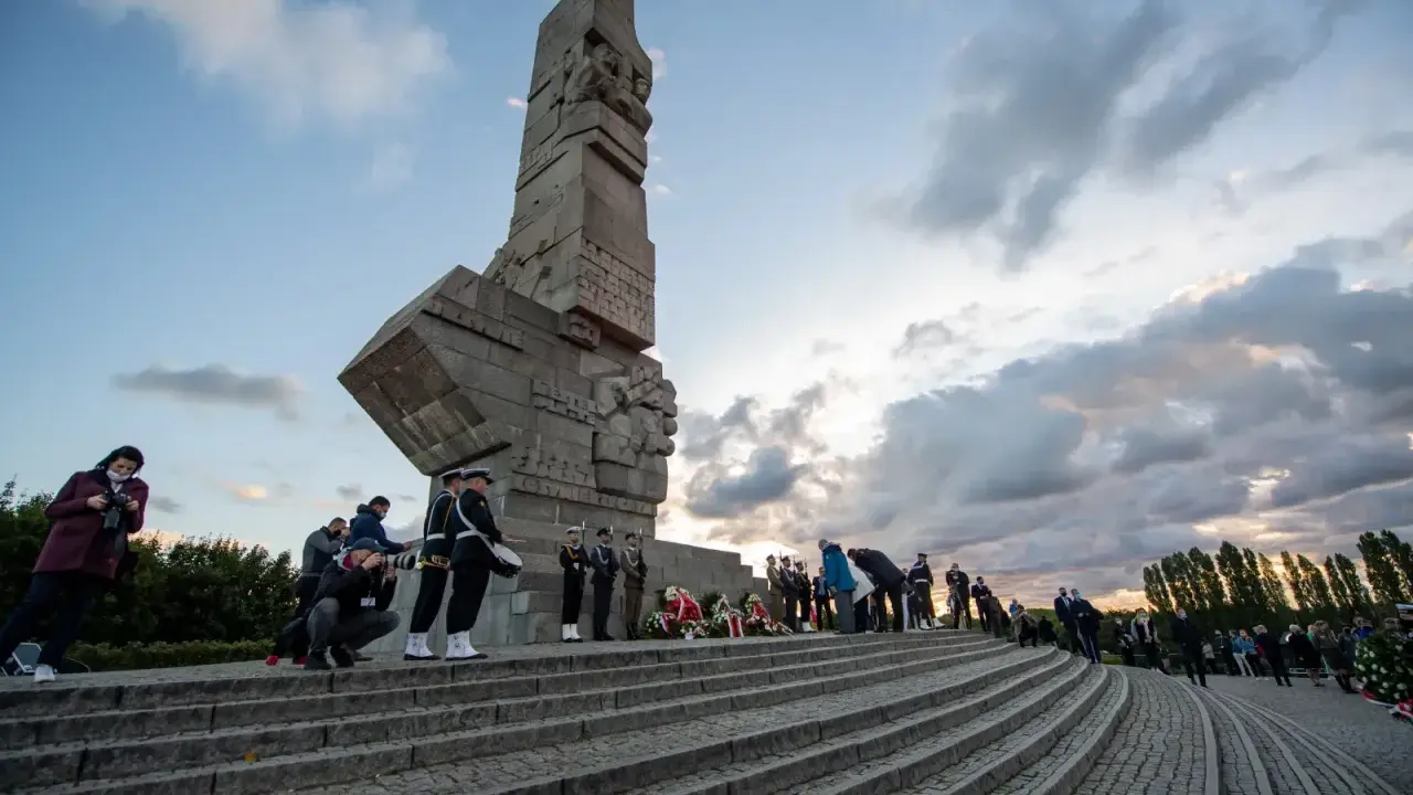 Uroczystość przy Pomniku Obrońców Wybrzeża na Westerplatte w Gdańsku. Warty honorowe, wieńce i zgromadzeni ludzie.