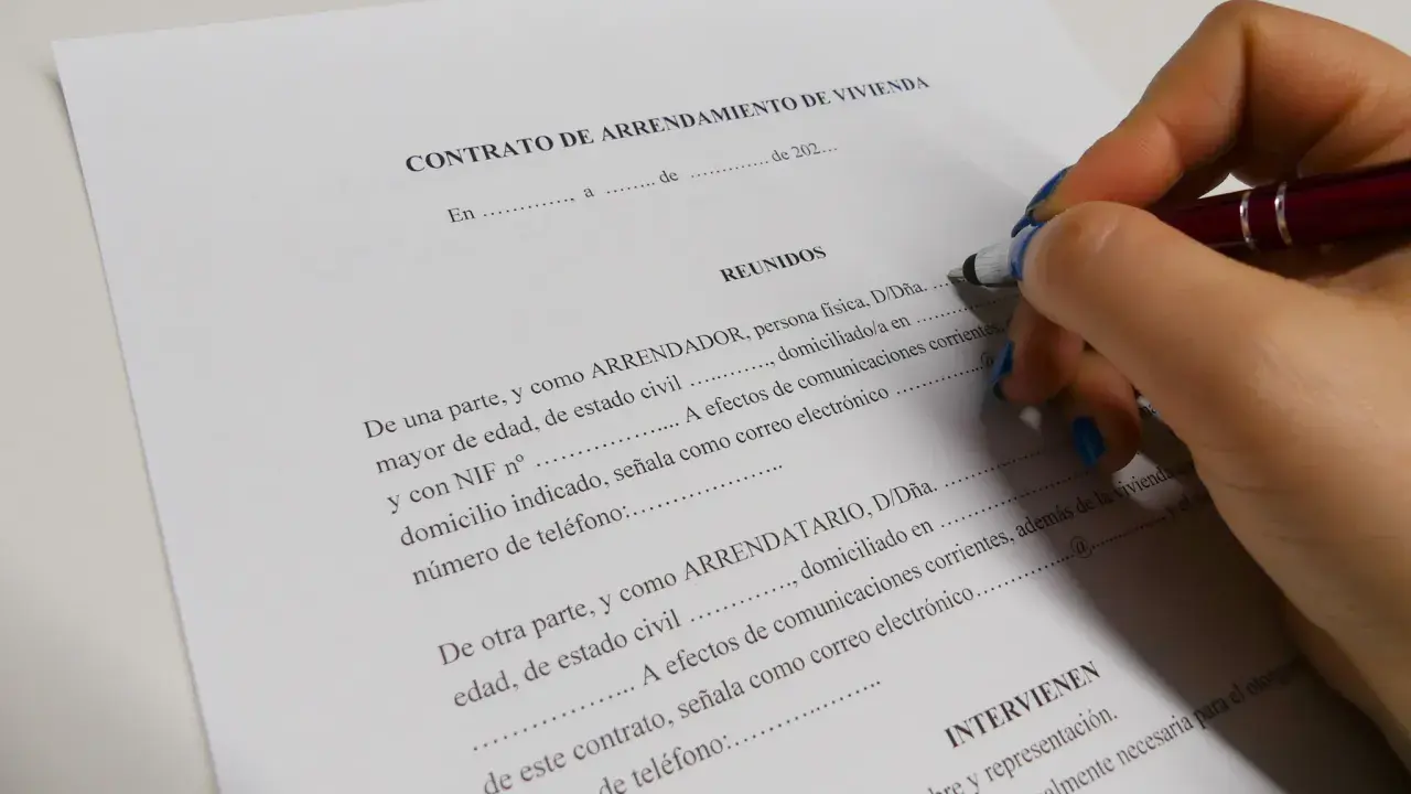 Mano con bolígrafo firmando un contrato de arrendamiento de vivienda, un documento legal clave.