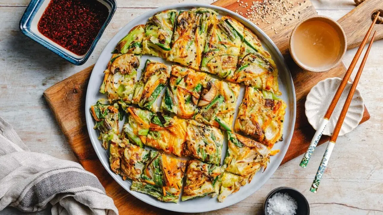 Bunte koreanische Pfannkuchen mit Gemüse, Pilzen und Karotten, serviert mit Dip und Stäbchen.