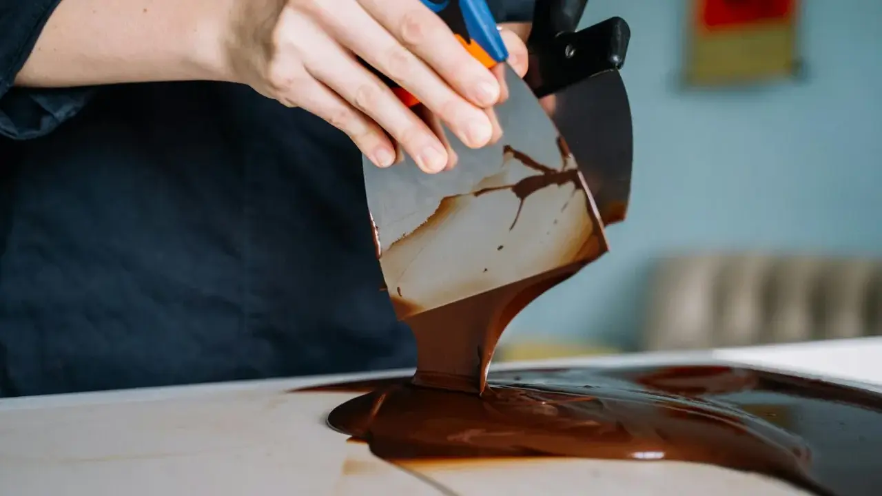 Mains travaillant du chocolat brillant sans tempérage avec des spatules. La texture fondante et lustrée promet une gourmandise parfaite.