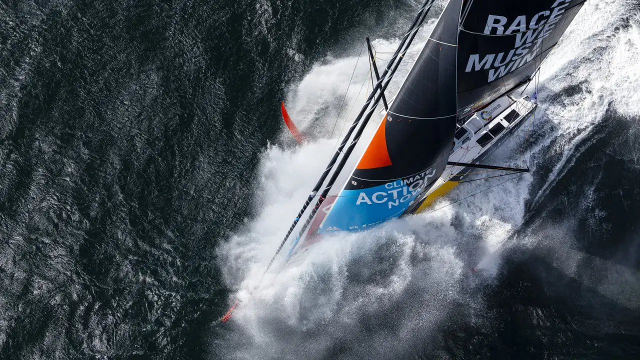 Le voilier de Boris Herrmann fend les vagues, projetant une gerbe d'eau. La voile arbore "Race we must win".