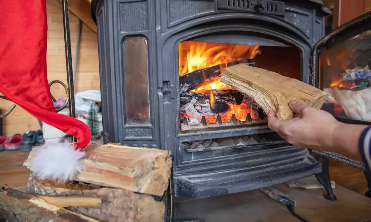 Une main ajoute du bois dans un poêle à bois allumé. Un bon choix de poêle à bois est essentiel pour un hiver chaleureux.