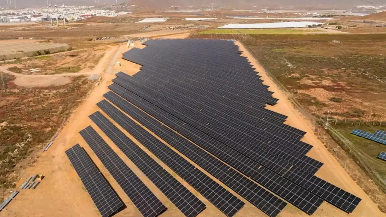 Große Solaranlage in Spanien, die die "Sonnensteuer" umgeht und saubere Energie liefert. Im Hintergrund Windräder und eine Stadt.