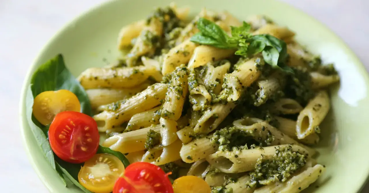 Penne z pesto i pomidorkami koktajlowymi. Pyszny obiad bez mięsa, udekorowany listkami bazylii.