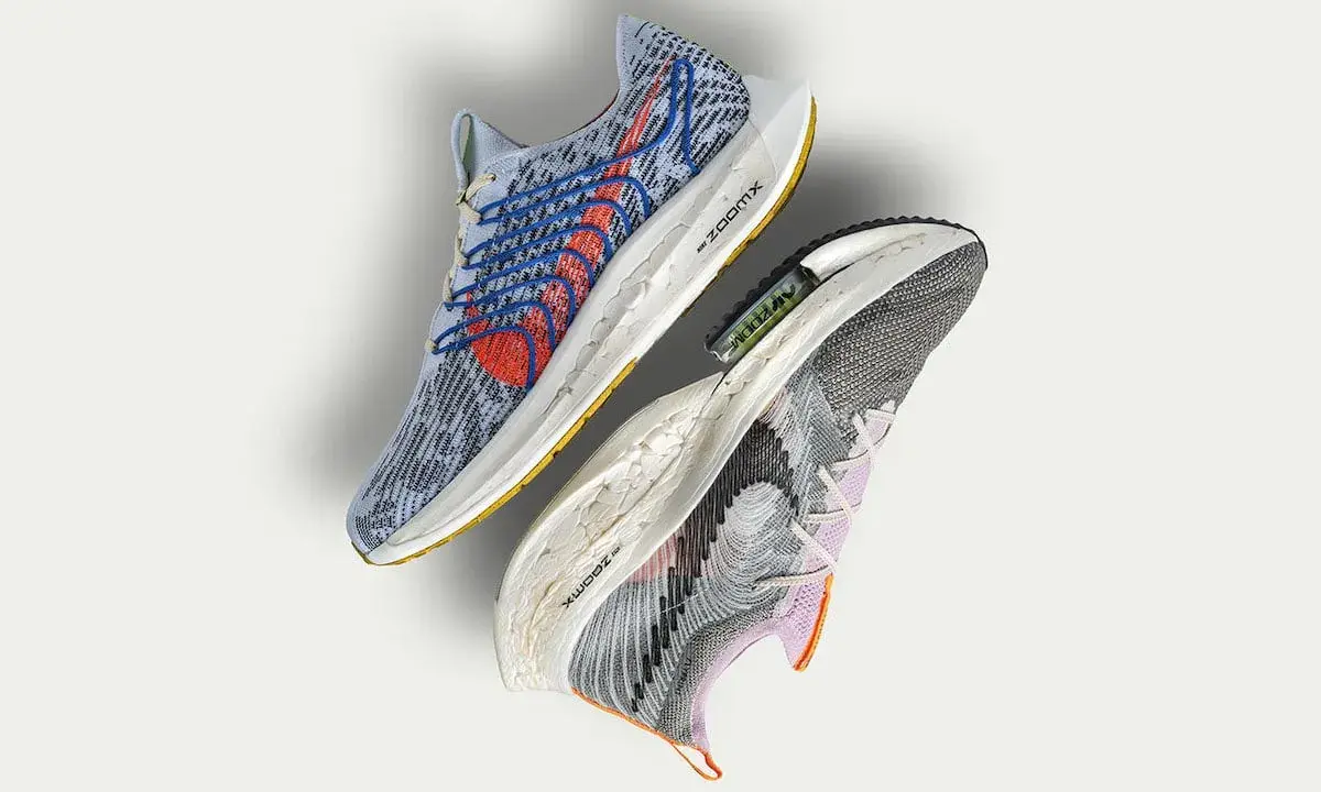 Dwa buty sportowe Nike, jeden niebieski z czerwonymi akcentami, drugi szaro-fioletowy. To przyszłość biegania z Nike Move to Zero.