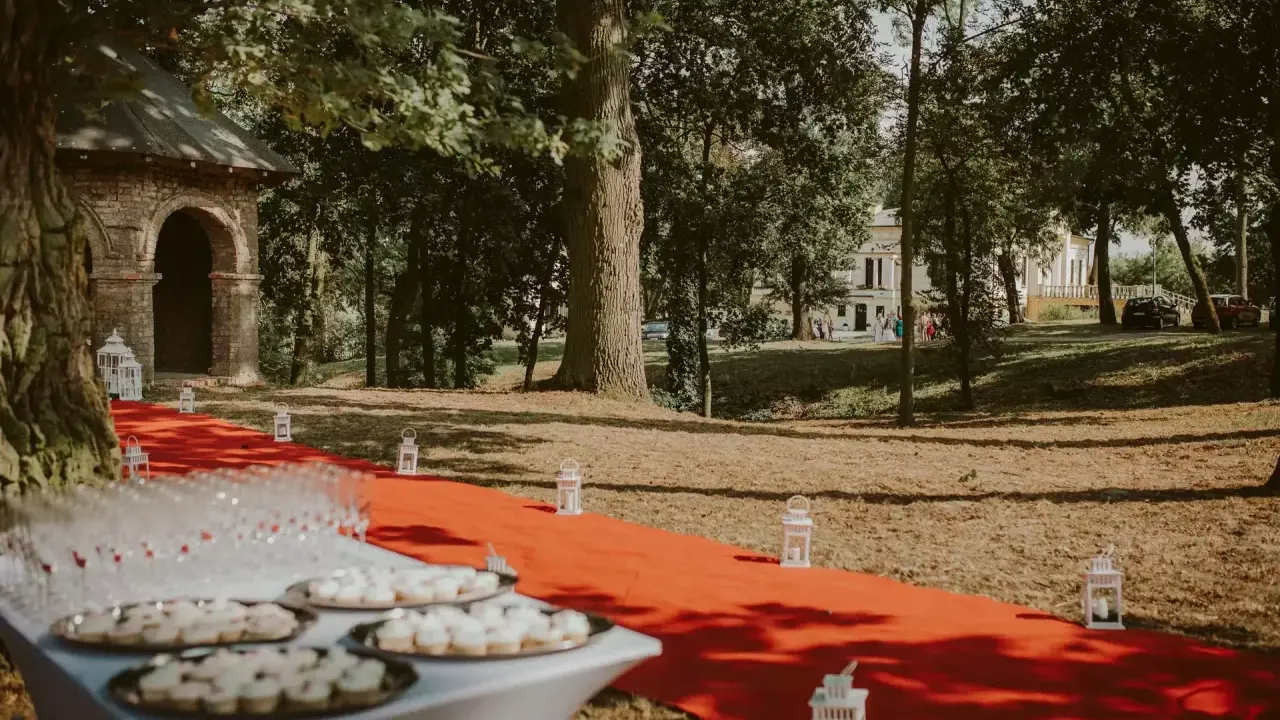 Czerwony dywan prowadzi do pałacu w Małkowie, ozdobiony lampionami i stołem z przekąskami.