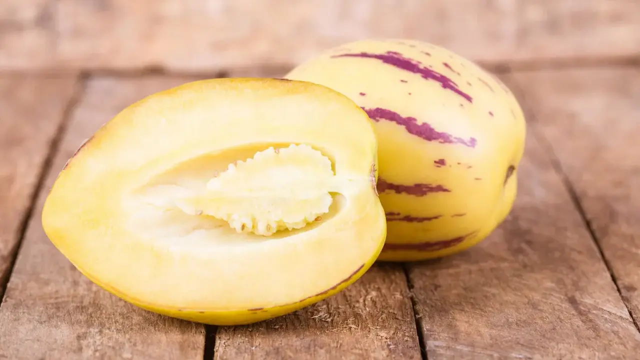 Eine Melonenbirne, die nicht giftig ist, wird auf Holzbrettern präsentiert. Eine Hälfte zeigt das saftige Fruchtfleisch.