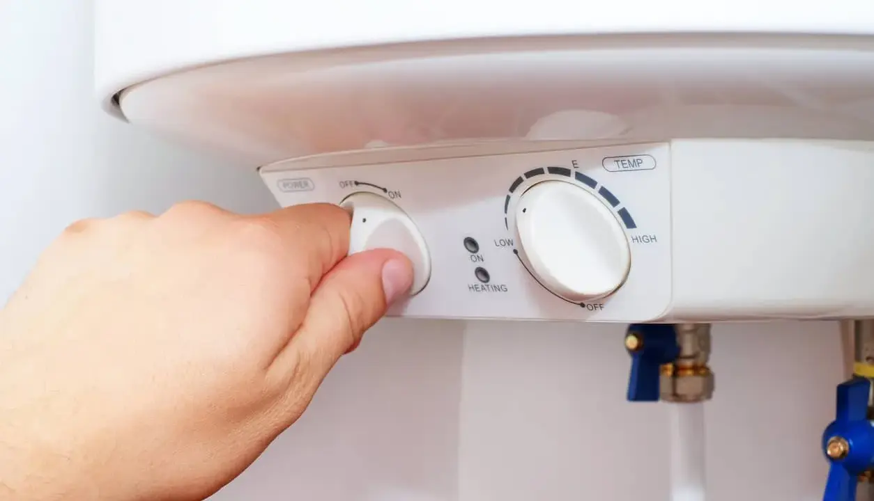Mano ajustando el dial de potencia de un termo eléctrico. Si el termo pita, puede ser por un ajuste incorrecto de temperatura o por un problema de calentamiento.