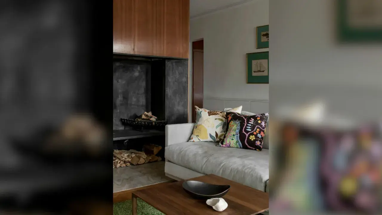 En soffa med färggranna kuddar framför en öppen spis med ved. En stilfull inredning som påminner om Josephine Blix design.