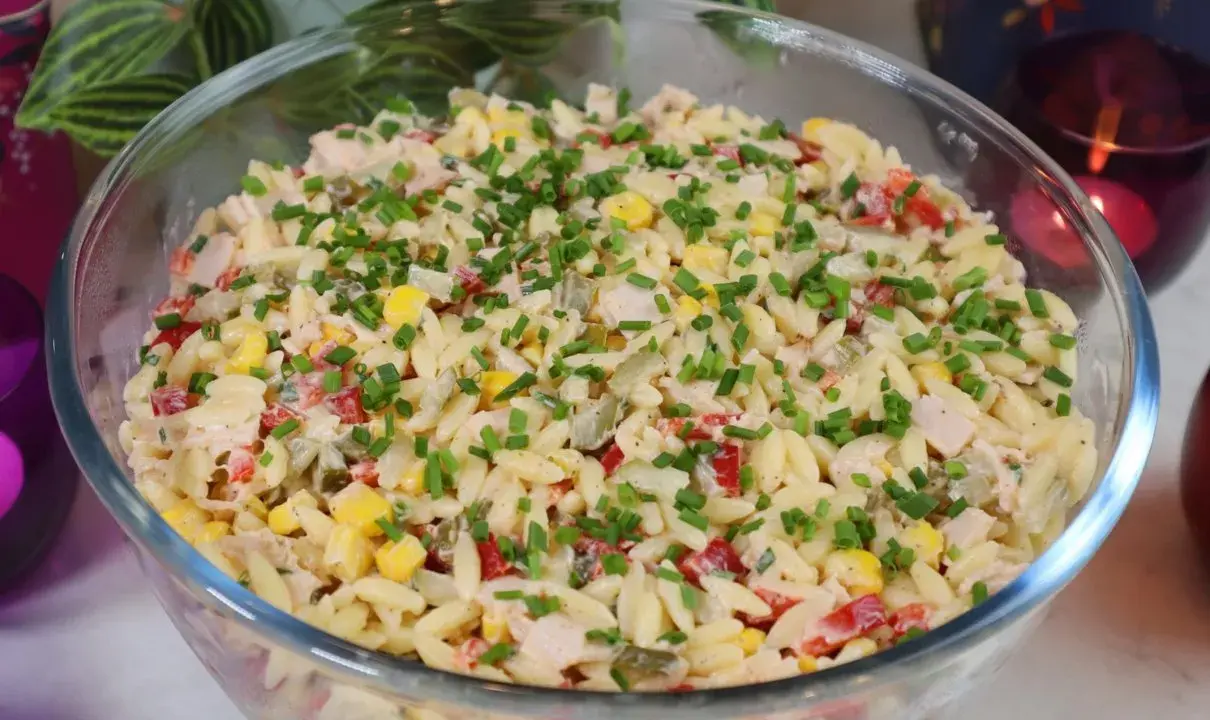 Pyszna sałatka z makaronem orzo, kukurydzą, papryką i kurczakiem, posypana szczypiorkiem. Idealna na letnie dni.