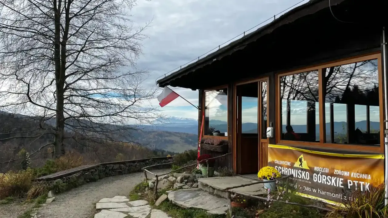 Bacówka pod Wierchomlą, schronisko górskie PTTK z widokiem na góry. Polska flaga powiewa nad wejściem.