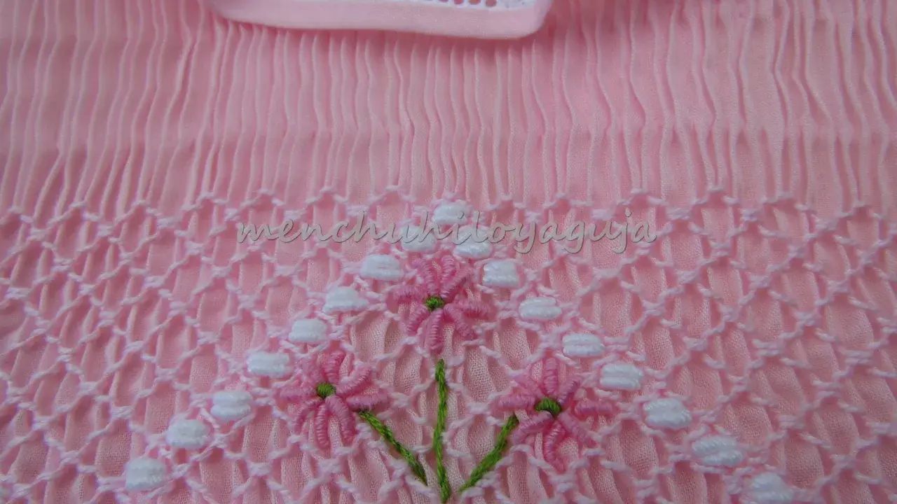 Detalle de puntada smock en tela rosa, con flores bordadas. Aprende como hacer punto smock.