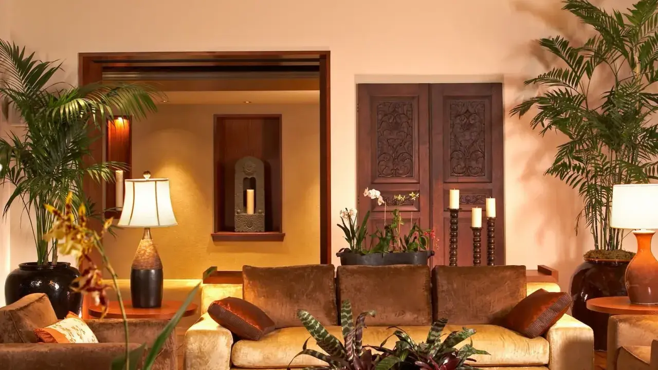Salotto accogliente con divani in velluto, piante tropicali e porte intagliate in legno scuro, che evocano un caldo **stile coloniale**.