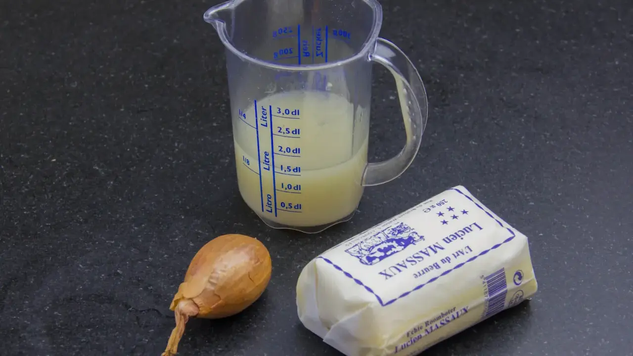 Ingrédients pour un beurre blanc : un oignon, un pichet gradué avec un liquide jaune, et un paquet de beurre Lucien Massaux.