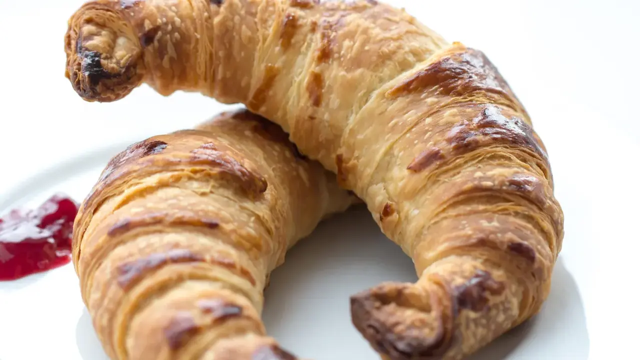Två gyllene croissants med vaniljfyllning ligger på en vit tallrik. En klick hallonsylt bredvid.