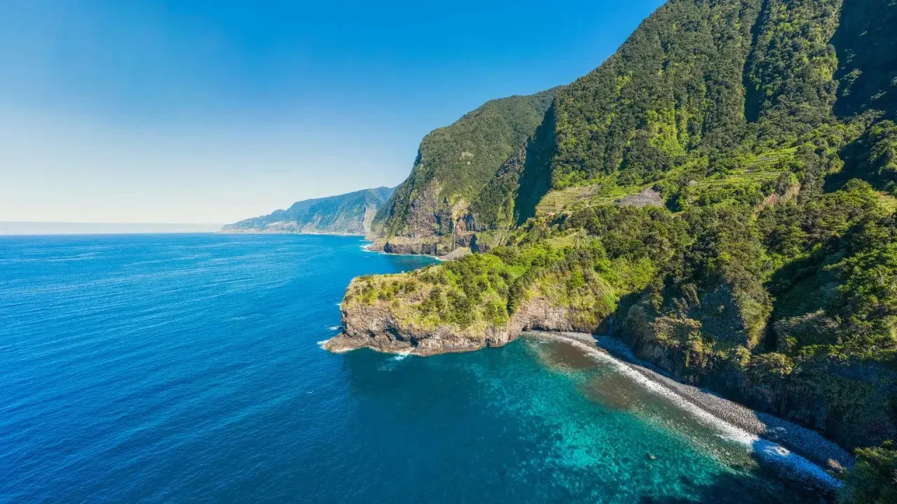 Grüne Berghänge stürzen ins türkisfarbene Meer. Ein perfekter Tag für eine Reise nach Madeira im Oktober.