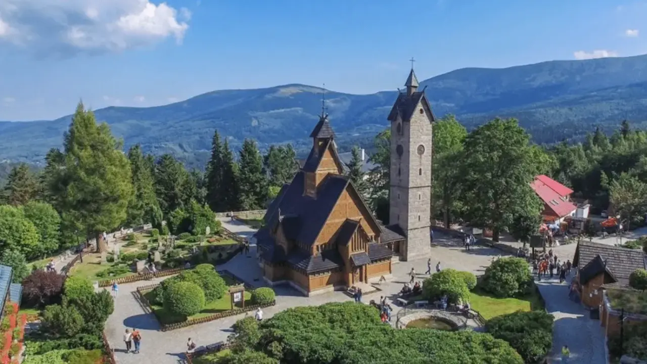 Drewniany kościółek i wieża na tle gór. Czy to Karpacz, czy Szklarska Poręba?