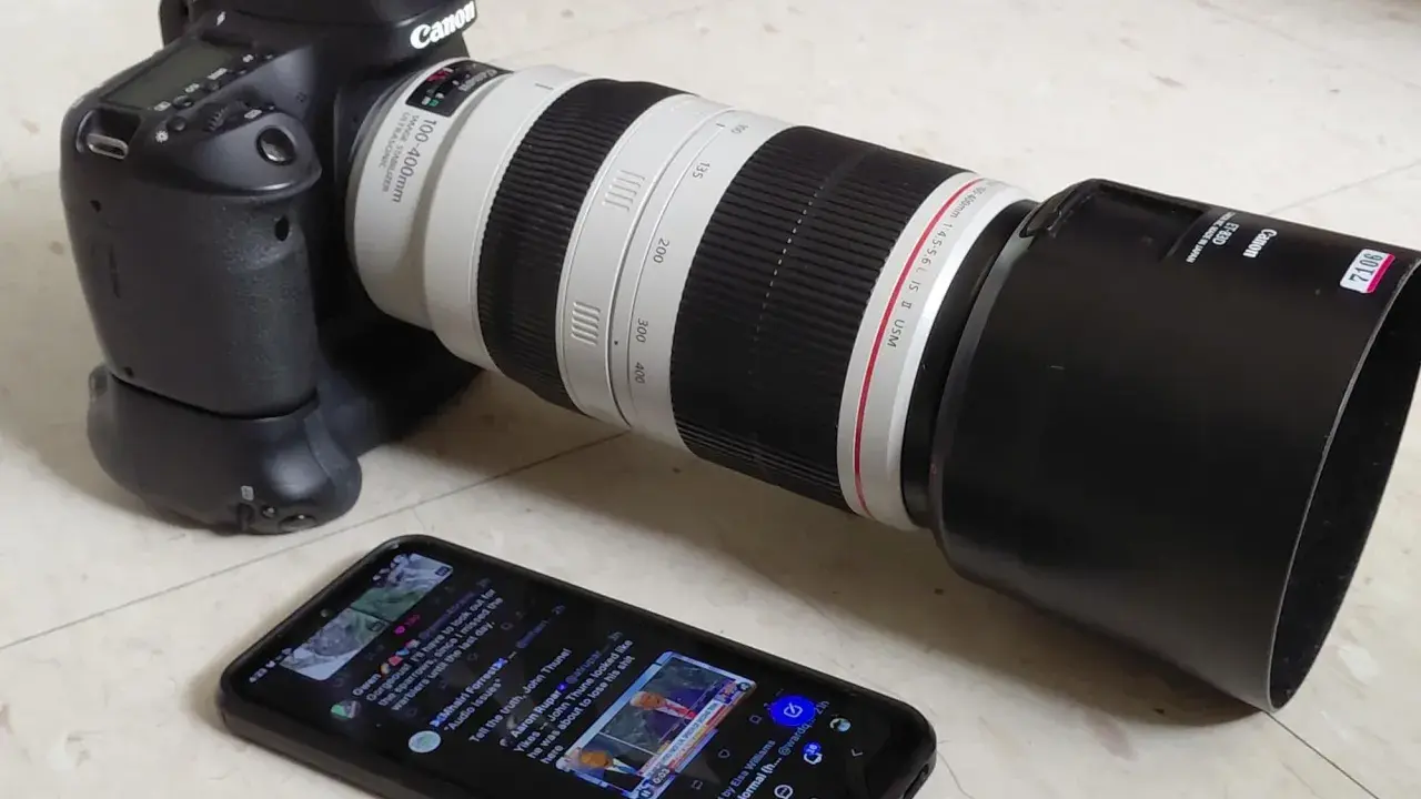 Canon 80D con obiettivo 100-400mm, pronto per una recensione. Sullo smartphone, un tweet su politica.