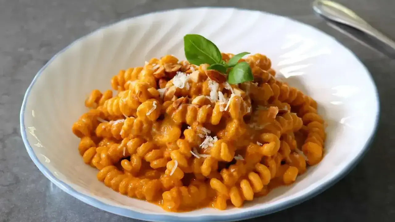 Szybki obiad z makaronem fusilli w kremowym sosie pomidorowym, posypany parmezanem i orzechami, udekorowany listkiem bazylii.