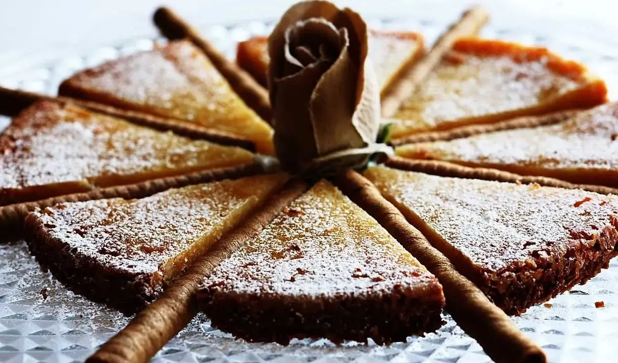 En vacker vit kladdkaka uppskuren i tårtbitar, dekorerad med en pappersros och chokladrullar.